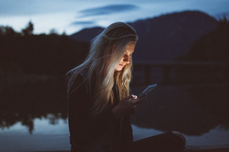 teen girl looking at phone in front of lake
