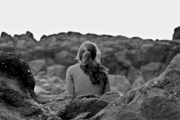 Girl sitting on rocks with back at camera