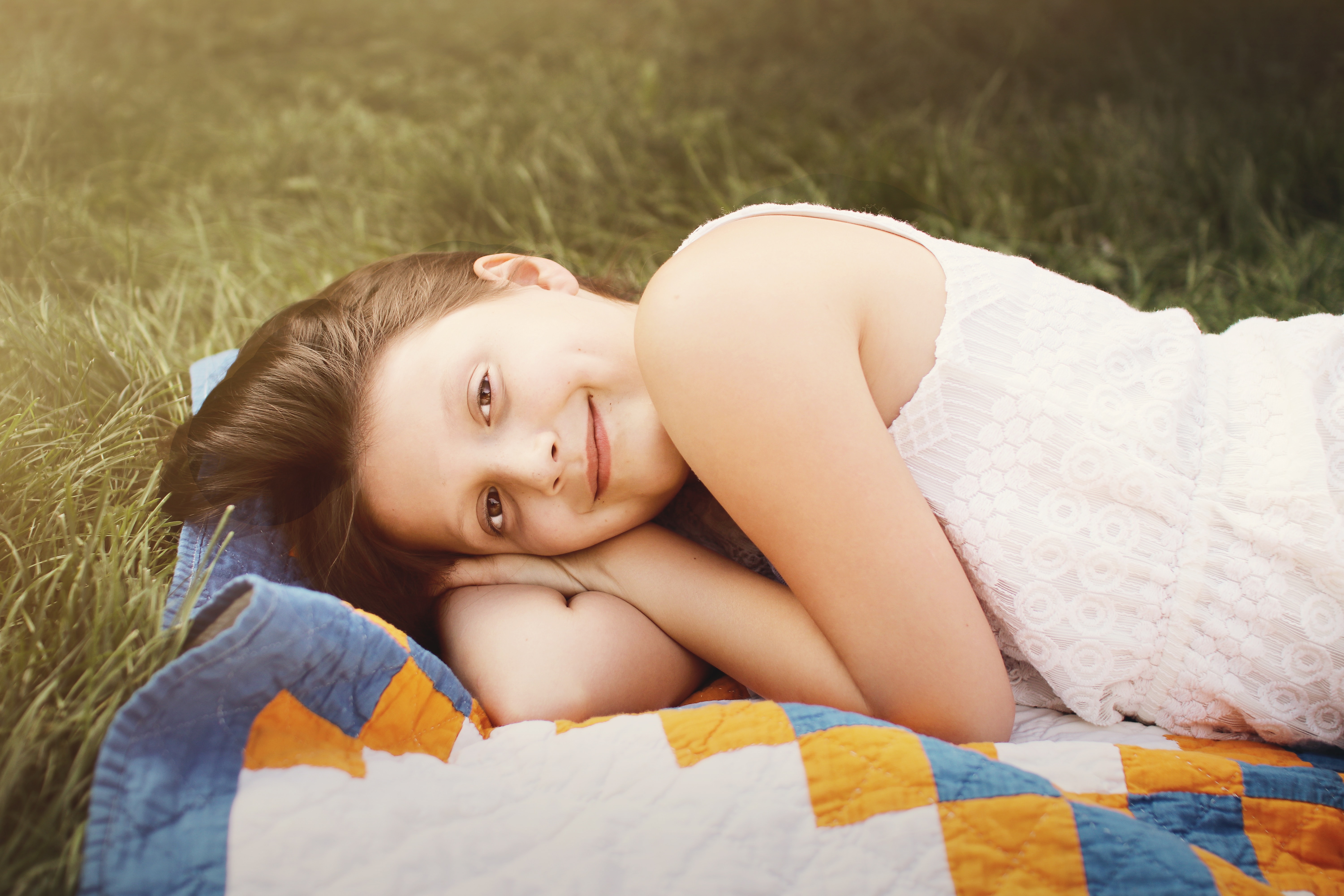 preteen girl lying on blanket in grass looking at camera