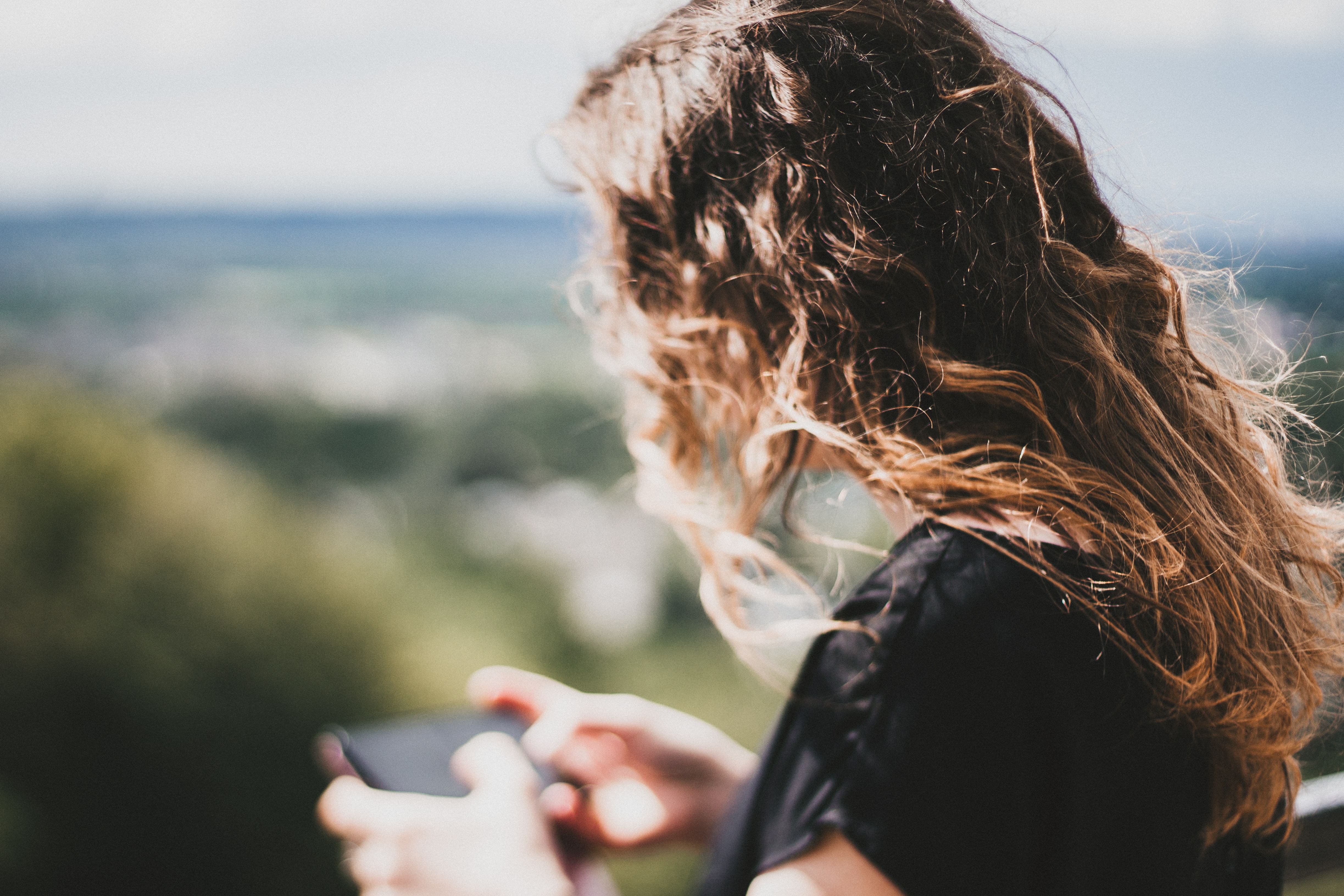 teen girl curly hair looking at phone in landscape